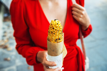 Woman in a red dress holds fried corn. Street snack.