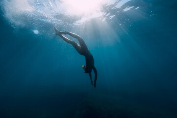 Silhouette of woman dive in transparent sea. Freediving with slim girl in ocean and sun rays
