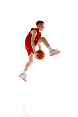 Full-length image of active teen boy in red uniform, basketball player training, playing isolated...