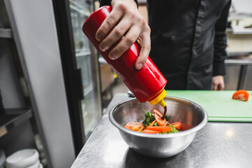 A hand squeezes a red condiment bottle over a bowl of vegetables, likely adding sauce or dressing