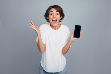 Naklejka premium Satisfied excited cheerful shouting woman with modern smart phone device in hand. Girl happy due to win in bet or lottery or in game, isolated on grey background