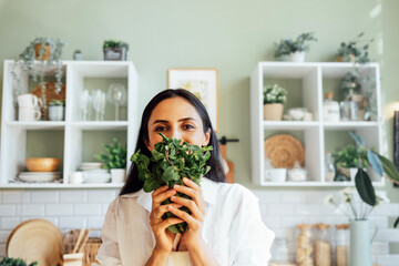 Attractive young woman stands in the kitchen and holds a bunch of fresh mint