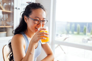 A smiling attractive Asian woman drinks freshly squeezed orange juice