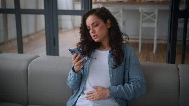 Caucasian woman girl female lady at home couch sofa stroking stomach belly tummy want eat order food delivery online cafe supermarket browsing mobile phone abdomen pain menstrual ache period pregnancy