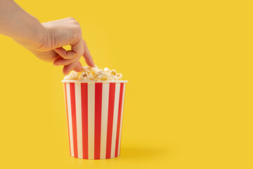 Hand takes popcorn from a striped box, theater film snack, crunchy treat, movie enjoyment.