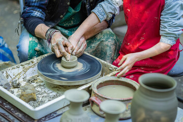 Man and a child are making pottery. The man is teaching the child how to make pot