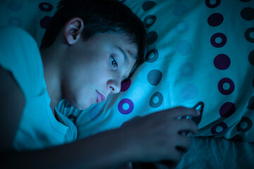 Boy addicted to smartphone insomnia problems surfing the internet or playing games at night in bed