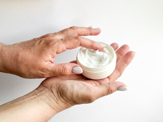 Close up of middle age woman hands holding container of cream and dipping finger on white background. Skincare and moisturizing concept. For healthcare, wellness, and self care poster.