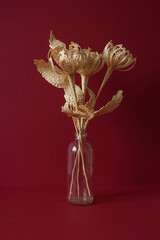 A glass vase with a bouquet of flowers made from straw on the red background. Straw weaving