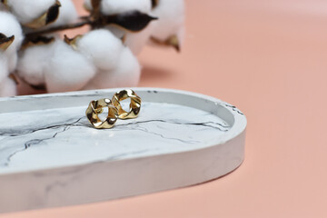 gold earrings in the old money style on a marble tray on a pink background decorated with dried flowers