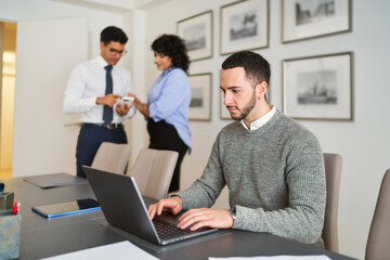 A man is typing on a laptop in front of a woman and a man