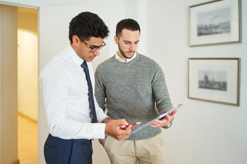 Two men are standing in a room, one of them is holding a clipboard