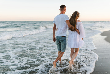 Barefoot on beach on water. Couple in love hugs on seashore. Female hugging male walking barefoot...