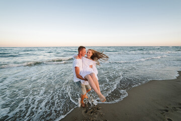 Man picks up his beloved woman in his arms holds it and twirls with her on beach. Couple have fun...