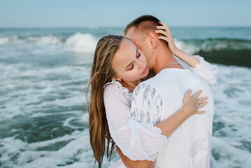 Swimming in clothes. Couple hugging and kissing in sea. Male kisses and hugs female standing on water with big waves ocean and enjoying a summer day. Portrait of a beautiful man and woman wet in sea.