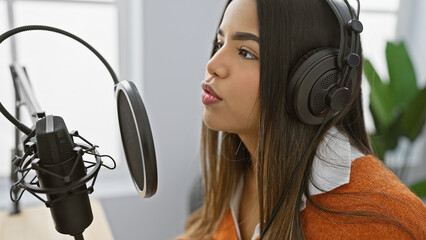 Hispanic woman with headphones speaks into microphone in a modern radio studio