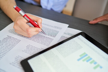 A person is writing on a piece of paper with a red pen