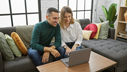 A smiling couple using a laptop together on a cozy couch in a modern living room setting.