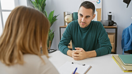 A man and a woman have a professional discussion in a modern office setting, suggesting they may be coworkers or a team.
