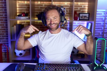 Middle age man with beard playing video games wearing headphones looking confident with smile on...