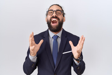 Hispanic man with beard wearing suit and tie crazy and mad shouting and yelling with aggressive...