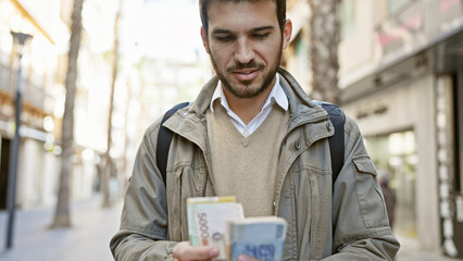 Handsome hispanic man counting korean won on a city street, highlighting urban life and travel.