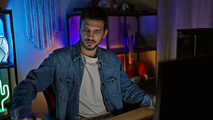 Handsome hispanic man with beard in a dark gaming room looking at screen, portraying a casual indoor setting at night.