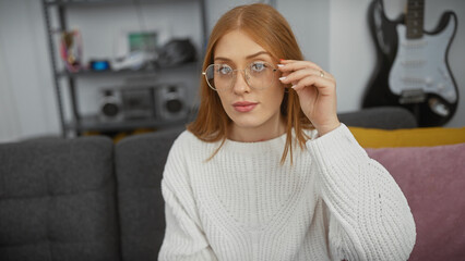 A stylish young woman adjusts her glasses in a modern living room, hinting at comfortable home life.