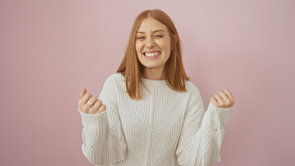 A joyful redhead young woman in a white sweater laughing against a pink background