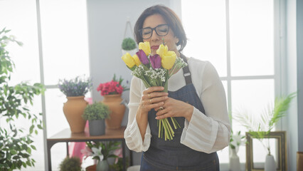 Mature woman smelling fresh tulips in a vibrant flower shop interior, conveying a sense of nature...