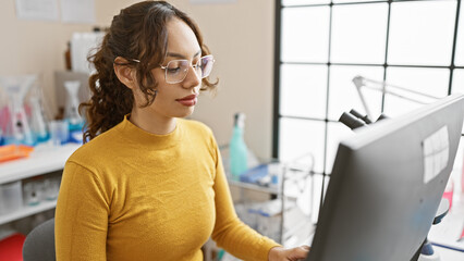 A young woman focuses on a computer screen in a well-lit laboratory setting, embodying...
