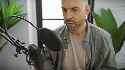 A focused man with a beard speaks into a microphone in a modern indoor studio.