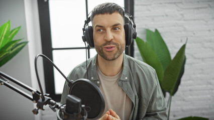 A handsome man with headphones speaks into a microphone in an indoor studio setting, capturing a...