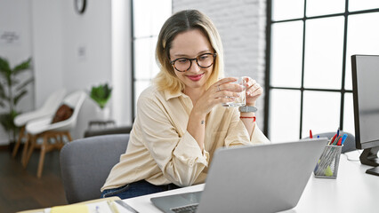 Fototapeta premium Young blonde woman business worker using laptop drinking water at the office