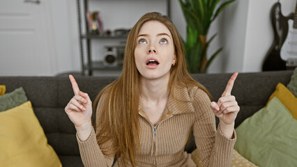 A surprised young woman points upwards in a modern living room, evoking curiosity and astonishment...