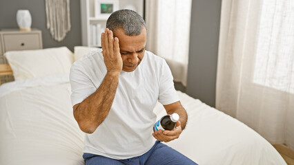 Mature hispanic man experiencing headache while holding medicine in a bedroom setting.