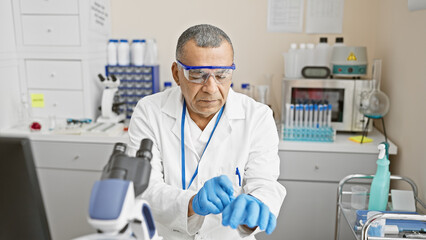 Mature hispanic man examines samples in a medical laboratory indoor setting wearing safety glasses...
