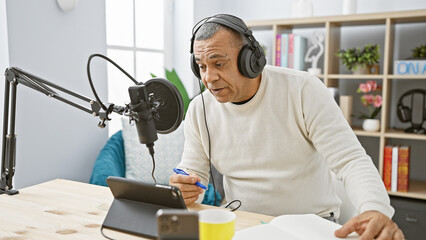 A middle-aged hispanic man in a radio studio setting with microphone and headphones, focused on his...