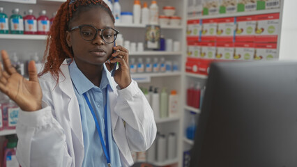 A young african american woman pharmacist multitasking in a drugstore while on the phone with...
