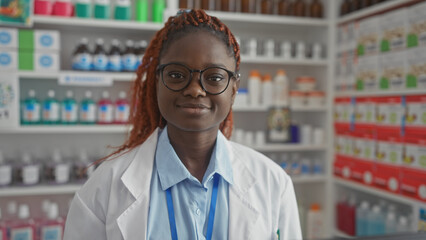 A cheerful young african american woman pharmacist stands confidently in a well-stocked pharmacy.