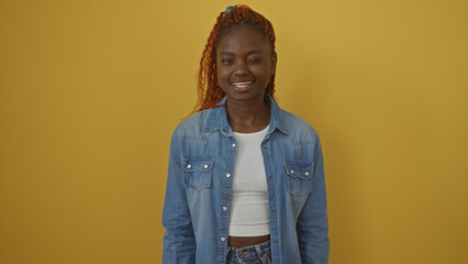 A cheerful young black woman in a denim jacket smiles against a vibrant yellow background.