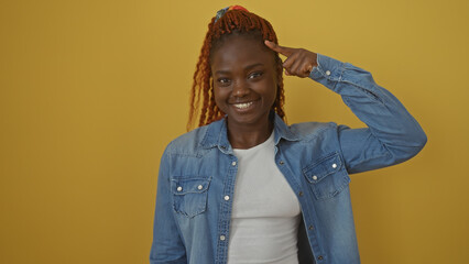 Smiling young african woman pointing to her head, isolated against a yellow background.