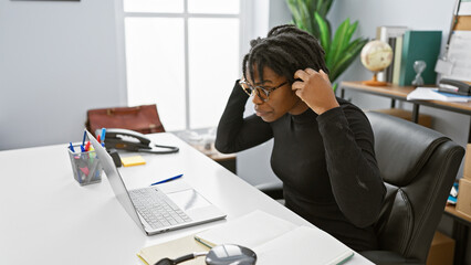 Focused african american woman with dreadlocks working at her office desk with a laptop and notebook.