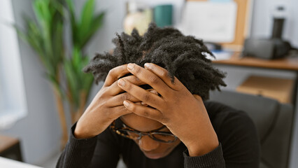 A stressed african american woman with dreadlocks sitting in an office room, showing frustration or...