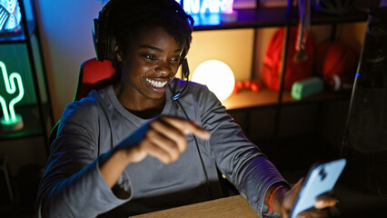 A smiling african american woman with headphones enjoys gaming at night in a home setting.