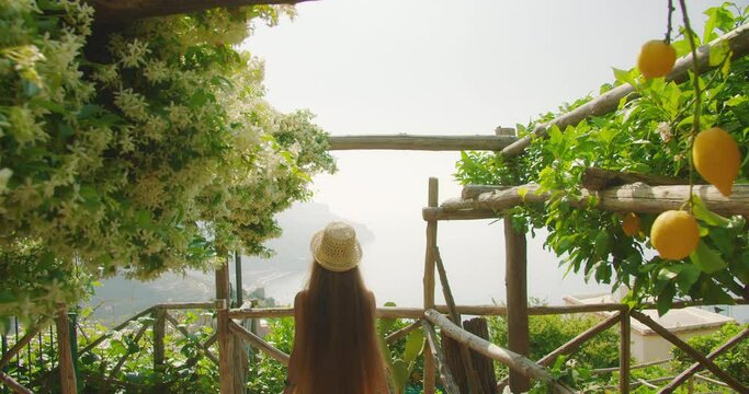 Woman enjoys a serene view of the Amalfi Coast from a terrace adorned with lemons. Tourist on summer holidays in Italy.