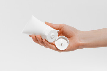 Female hand holding white open cream tube mockup on white isolated background. The concept of beauty products, applying cosmetics to the skin, daily nutrition and hydration.