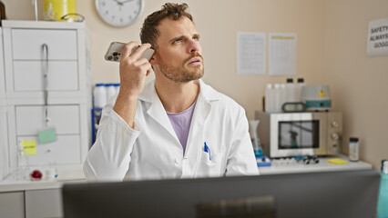 Young hispanic man with beard listens to voicemail in a hospital lab, showcasing a mix of concentration and concern.