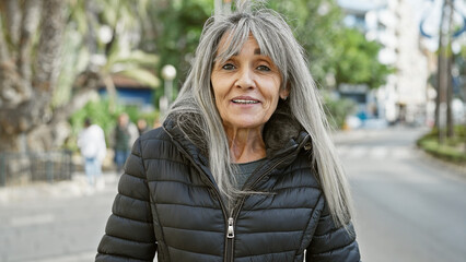 Mature hispanic woman with long grey hair smiling on a city street.