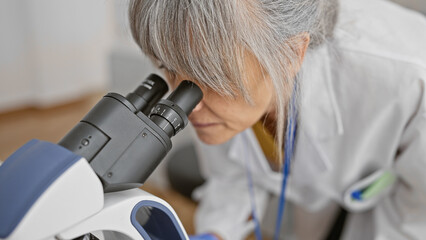 Mature woman scientist using a microscope in a laboratory setting, showcasing expertise and...